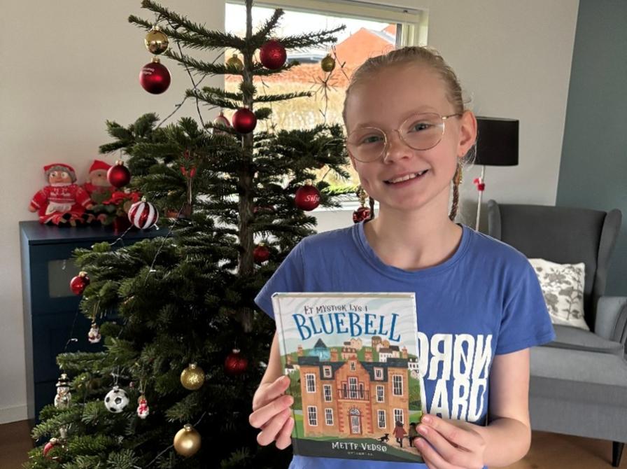 Læseagent Freja med bogen foran et pyntet juletræ